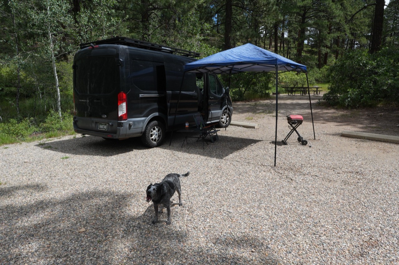 A camper van, canopy, chair, and dog at a Colorado campsite